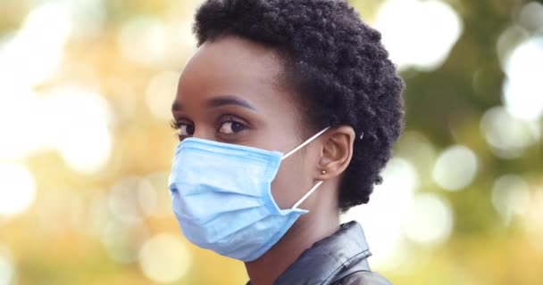 Portrét krásné Afroameričanky, jak se dívá jinam a obrací hlavu k fotoaparátu, nosí modrou lékařskou ochrannou masku. Close up na pěkný etnický maskované dívka v karanténě venku — Stock video