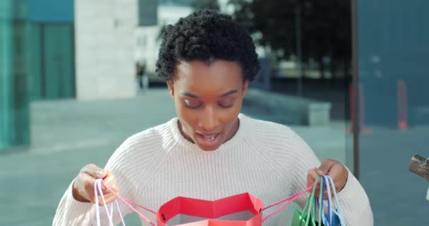 Удивлен энтузиазм радостной женщины африканский американец девушка афро смешанной расы студент покупатель потребитель ищет в сумке с одеждой подарки говорит вау открытый рот шокирован глядя на концепцию продажи камеры — стоковое видео