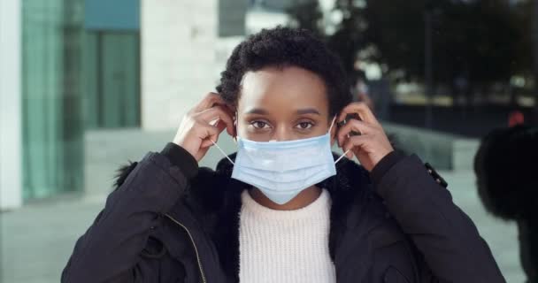 Retrato de mujer afroamericana caminando en la calle en los puestos de otoño posando para la cámara durante la cuarentena se pone máscara médica en su cara mostrando como poner el pulgar hacia arriba, apoyo aprobación signo de cerca — Vídeo de stock