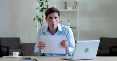 Genç işletme öğrencisi patron evrak masasında oturur, el üstünde dans eder, iş gününün sonunu kutlar, belgeleri havaya atar, aktif olarak evde hareket eder, erkek portresi ön görünümü