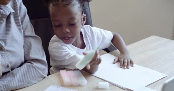 Famille deux personnes maman africaine ou nounou soeur aînée professeur aider enfant fille américaine fille enseignement tout-petit enfant apprentissage dessin coloriage image avec crayons marqueurs ensemble, activité créative — Video