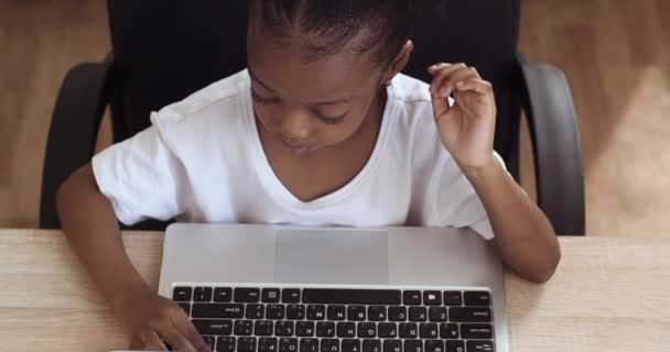 Ovanifrån rolig söt svart barn afrikansk förskola flicka dotter skriva på bärbar dator tangentbord spela online studera arbeta hemifrån tittar på kameran vänliga vinka hej för hand — Stockvideo