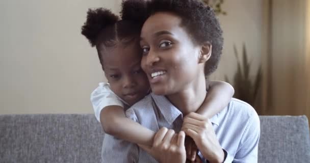 Портрет двух человек африканской мамы и милая маленькая дочка разговаривает смеясь улыбаясь обнимаясь сидя в гостиной диван. Ребенок обнимает маму за ее спиной любящей концепции семьи — стоковое видео