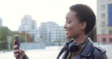 Genç Afrikalı kız arkadaşlarıyla video konferansında sohbet ediyor. Akıllı telefon aygıtı, telefona cevap verme, modern medya konsepti, yan görüş kullanıyor. Telefon ağında gülümseyen mutlu kadının portresi