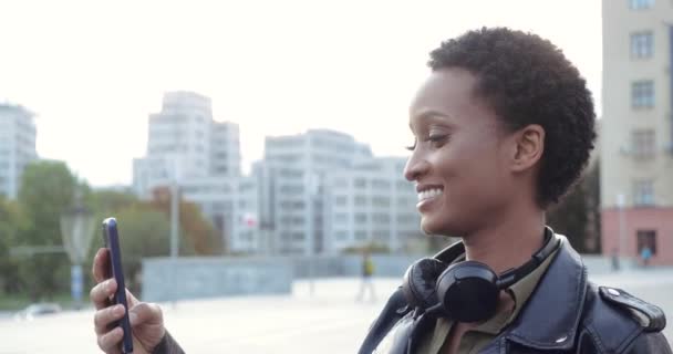 Joven adolescente africana chateando en una videoconferencia con amigos usando un dispositivo inteligente, respondiendo llamadas, concepto de medios modernos, vista lateral. Retrato de mujer feliz sonriente hablando en la red telefónica — Vídeo de stock