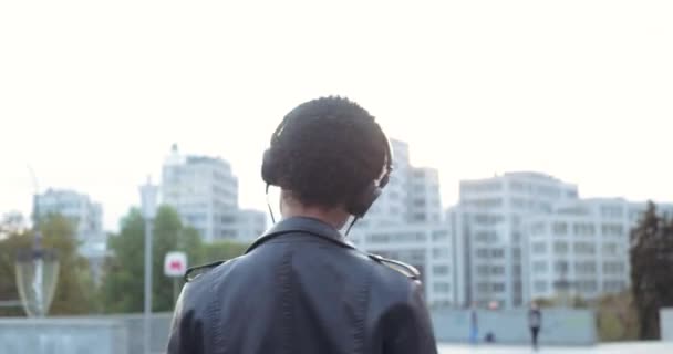 Портрет самотньої африканської дівчини - музиканта слухає пісні з навушниками на вулиці, рухає її тіло ритмічно виглядає спокусливо в камері, стоїть на міському фоні. — стокове відео