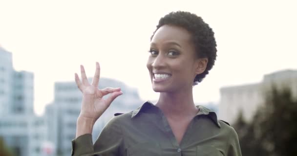 Porträtt av aktiv glad afrikansk flicka står poserar framför kameran ler med vita tänder känns tillfredsställelse, höjer handen upp, visar okej gest, viker fingrarna till noll, symbol för samtycke seger — Stockvideo