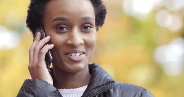 Portrait d'une femme satisfaite d'origine américaine parlant sur un téléphone portable avec des amis se réjouissant en souriant dents blanches à l'extérieur. Mixte fille de course étudiant fait une commande en ligne sur smartphone — Video