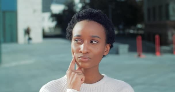 Retrato de mulher africana em pé branco ao ar livre perto do edifício da cidade coloca o dedo para enfrentar lembrando pensar sobre a ideia. Tiro de cabeça de brooding raça mista étnica menina estudante planejamento — Vídeo de Stock