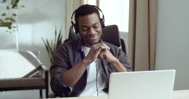 Ritratto di afro americano nero uomo d'affari freelance studente seduto a casa ufficio tavolo sul posto di lavoro indossa cuffie testa microfono ascolta musica online in laptop danza si muove mani per audio — Video Stock