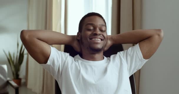 Portret van vrolijke kalme Afro-Amerikaanse jongen student zakenman freelancer baas programmeur zitten aan tafel op het werk in huis kantoor met gevouwen handen achter zijn hoofd rusten ontspant tijdens de pauze — Stockvideo