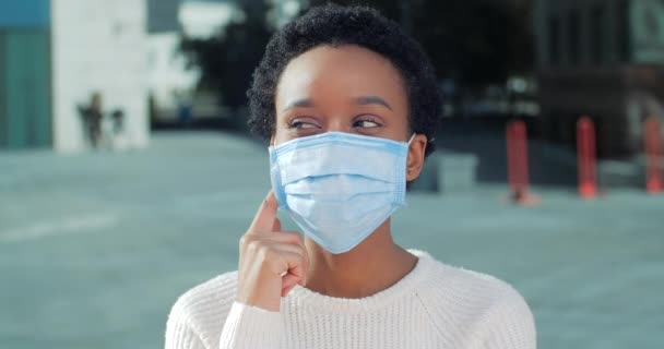 Портрет задумчивой афроамериканской девушки в медицинской защитной маске думает, что помнит делает выбор, держа подбородок пальцами и рукой, пациентка стоит на улице во время вирусной пандемии — стоковое видео