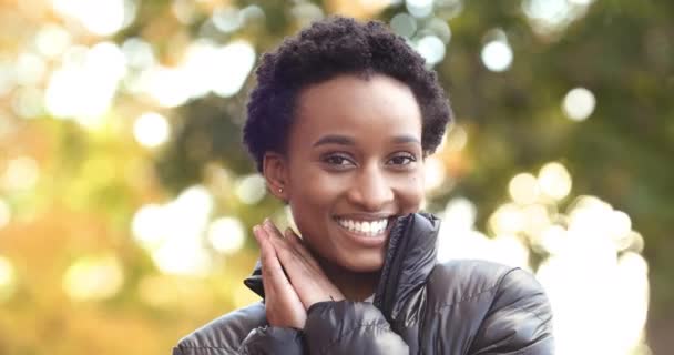 Portrait de fille afro-américaine femme noire debout dans la rue en automne à l'extérieur coquet posant en regardant la caméra souriant dents riant profiter de la jeunesse temps chaud plie les mains près du visage féminin — Video