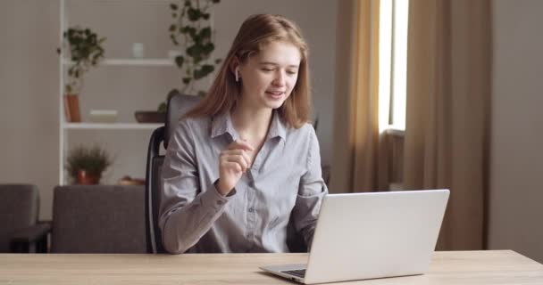 Retrato de estudiante sentada en casa lleva auriculares habla con el profesor en línea a través de la cámara web portátil, estudios sobre e-learning, habla con amigos gesticula activamente, muestra con sus manos — Vídeos de Stock