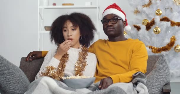 Pareja afroamericana sentados juntos en el sofá y viendo televisión comediante cine película comer palomitas de maíz descansando relajante en casa durante las vacaciones de Navidad en el interior del apartamento decorado, feliz año nuevo — Vídeos de Stock