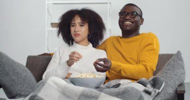 Afro-Amerikalı erkek ve genç kız kanepede oturmuş televizyon seyrediyor programdan memnun olmayan kadın kocasının komedi güçlerinden erkek arkadaşına gülüp kanalı değiştirmesini anlamıyor.
