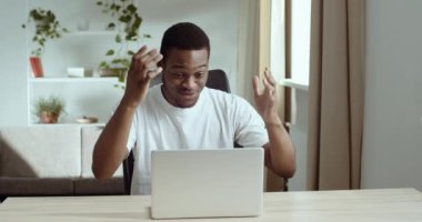 Mutlu şevkli afro-amerikalı adam beyaz günlük tişört giyiyor masaya oturuyor dizüstü bilgisayar ekranına bakıyor olumlu sınav sonuçları okuyor iyi haberler öğreniyor büyük ikramiye, başarı konsepti