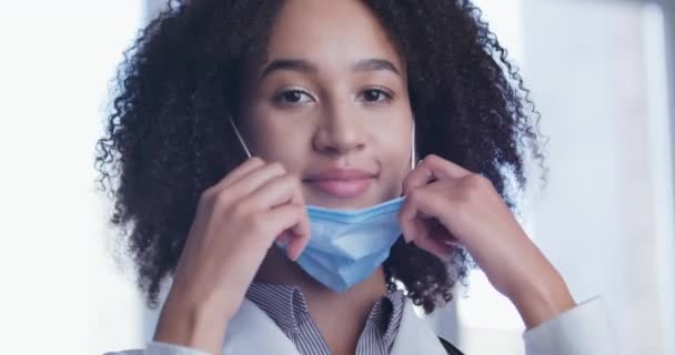 Portrait of African foreign student young medical intern, aspiring nurse stands posing in front of camera, puts on protective mask from face, smiles happily after hasty exam or patient consultation — Stock Video