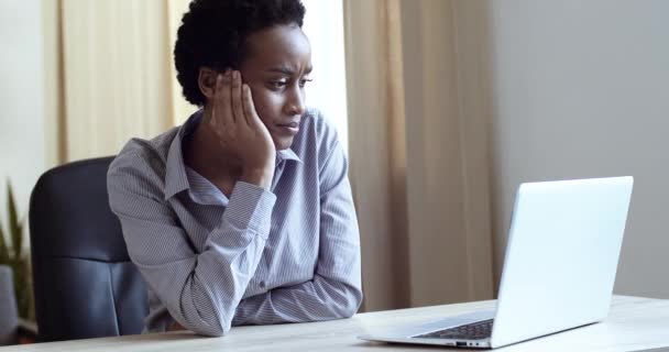 悲しい疲れアフリカの女性はオフィスでノートパソコンを働いています。不幸な女性は自宅でコンピュータ技術を使用しています。心配する混合レースの女の子はフリーランスの仕事でストレスを感じています。ビジネスの女性が画面を見て動揺 — ストック動画
