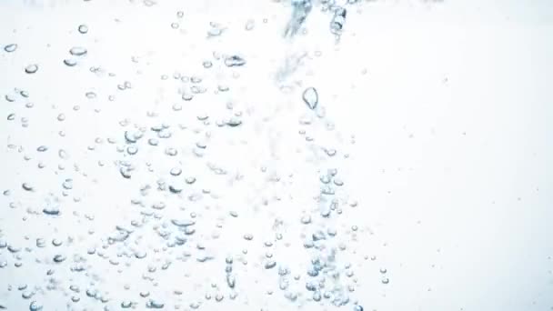 El chorro de agua en cámara lenta cae sobre una superficie lisa y limpia, creando burbujas de aire, salpicaduras de gota después de caer. Frescura de un líquido azul claro vertido en un recipiente transparente sobre fondo blanco — Vídeo de stock