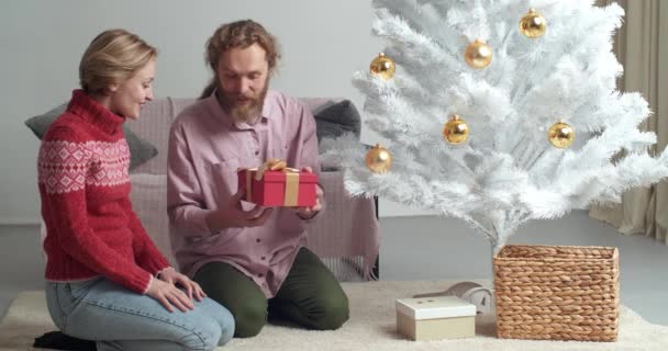 Kaukasische liebevolle fürsorgliche Ehemann Freund bärtigen Mann gibt seiner Frau Freundin schöne Frau Weihnachtsgeschenk rote Geschenkbox, Mädchen schüttelt Paket fühlt Freude sagt wow öffnet Mund in Überraschung — Stockvideo