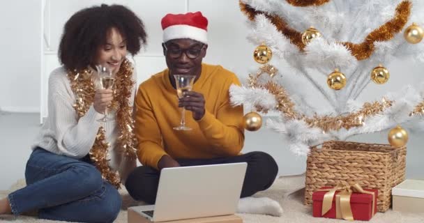 Capodanno durante la pandemia coronavirus, coppia afro-americana donna e uomo celebrano a casa seduti vicino all'albero di Natale bere champagne indossare vestiti festivi parlare online video conferenza riunione remota — Video Stock