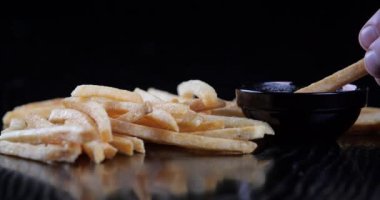 Erkek eli kızartılmış altın sarısı patates kızartması Amerikan fast food 'u kırmızı domates sosuna batırılmış kırmızı ketçap, iştah açıcı çerçeve, siyah tabak ve siyah masada lezzetli yemek standı.