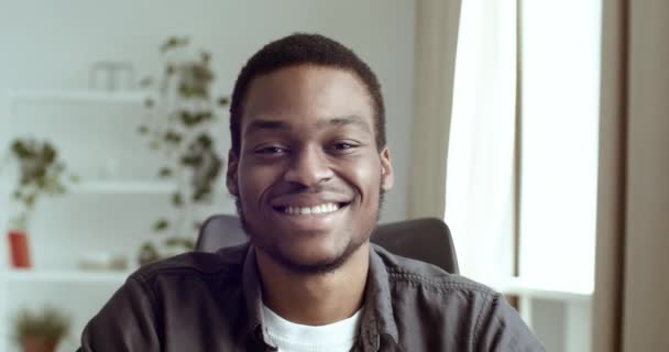 Портрет усміхненого чорношкірого чоловіка африканського студента бізнесмена, який сидить за столом в офісі вдома, дивлячись на камеру, показуючи два пальці другого номера жест мир схвалення доброзичливість привітання — стокове відео