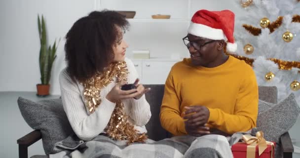 Afro americano hombre negro chico marido hermano novio amigo dando nuevo año pequeño regalo caja regalo de Navidad esposa novia rizado mezclado raza chica, 2021 año nuevo celebración en casa aislado en sofá — Vídeo de stock
