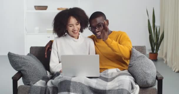 Jovens negros sorrindo casal misto raça étnica afro-americana recém-casados marido e mulher namorado e namorada sentar no sofá em casa sala de estar fazendo videochamada conferência de bate-papo on-line em pandemia — Vídeo de Stock