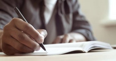 Yakın plan erkek el ele tutuşma kağıdı kağıtlarına not alır. Kırpılmış çerçeveli Afro-Amerikan bir adam kalem raporu ile yazı yazıyor ana hatlarıyla çalışıyor evde çalışıyor, masada oturuyor.