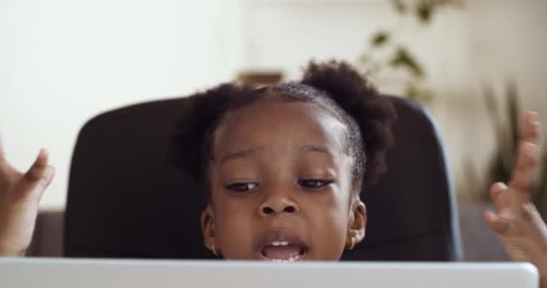 Retrato de olhos infantis espreitando por trás do laptop. Pequena menina afro-americana senta-se no computador lutando com problema sente estresse frustrado pelo fracasso na lição de casa estudando remotamente de casa — Vídeo de Stock