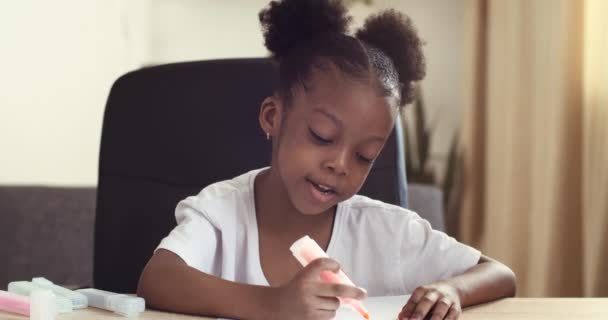 Afro-Amerikan ırkının aktif, neşeli kızı keçeli kalemli kırmızı pembe kalemle resim çiziyor, resim çizimlerinden bahsediyor, evde uzaktan yakından ilgilenen yetenekli etnik kökenli çocuk. — Stok video