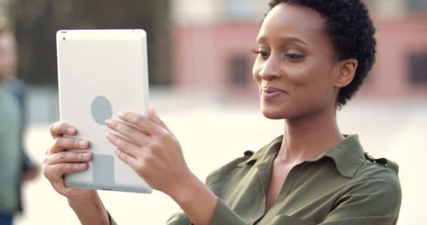 Ethnique jeune femme tient tablette d'ordinateur dans ses mains dispositif numérique moderne, parle regarde en webcam, conférence en ligne, répond appel sur le réseau, prend la vidéo pour blog, tête de vague en accord de près — Video