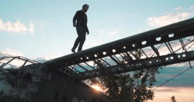 Parçalanmış eski bir Sovyet mısır uçağının kanadında yaz akşamında gün batımına doğru yürüyen meraklı erkek turistin alt görüntüsü. İlham verici bir adam terk edilmiş bir havaalanının uçan nakliye aracına tırmanır..