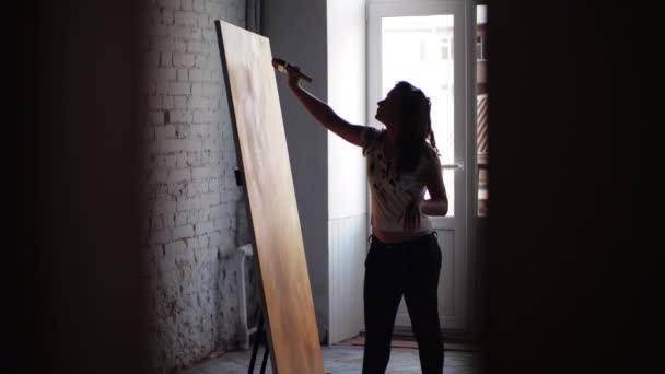 Artysta emocjonalnie tworzy arcydzieło abstrakcyjnego malarstwa w studio przed oknem. Kobieta używa szerokiego pędzla, farby olejnej. Dziewczyna łącząca różne techniki w kreatywności. — Wideo stockowe