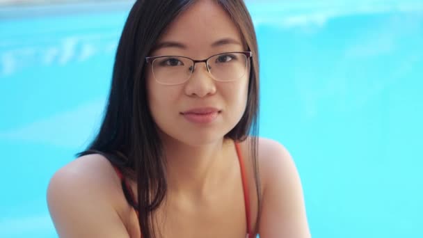 Vista de perto da etnia asiática colocada senhora em óculos sentados à beira da piscina no spa do hotel em casa, resposta positiva na pergunta comunicar, acordo balança a cabeça, olha para a câmera com endosso — Vídeo de Stock