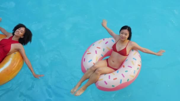Two young teenagers girls exchange students spend weekend together two persons in pool, swimming on inflatable sits ring, sunbathing in bikini, laughing, talking friendly, smiling, friendship concept — Stock Video