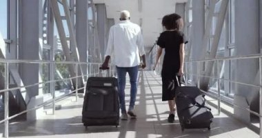 Arkadan bakıldığında tam boy Afro-Amerikan çift karışık ırk arkadaşları karı koca yabancı öğrenciler havaalanında birlikte yürüyorlar tren istasyonunda bavullar, seyahat konsepti taşıyorlar.