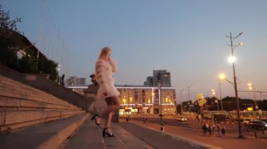 Çekici genç sarışın siyah topuklu ve beyaz elbiseli merdivenlerden inip şehir merkezi Kharkov, Ukrayna 'da saçını düzleştiriyor. Çekici bir modelin akşam yürüyüşü