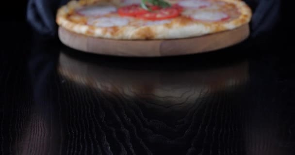 Primer plano del hombre lleva guantes de látex negro camarero hombre manos sirven traer a la mesa apetitosa pizza vegetariana caliente con presentación plato de queso mozzarella en el concepto de pizzería de restaurante de tablero de madera — Vídeo de stock