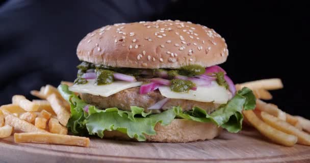 Vágott keret, sakk burger marhahús paradicsom salátával áll a fekete asztal fa fórumon. Egy közeli kép a zsíros, szaftos gyorskajás hamburgerről, amit a pincér séf szolgál fel. Egészségtelen amerikai sült krumpli — Stock videók