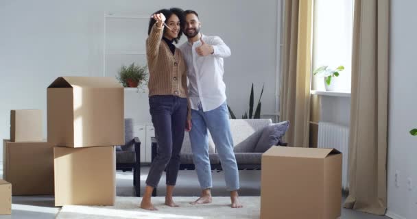Para Afrykańczyków rasy mieszanej czarny kobieta dziewczyna i biały mężczyzna mąż chłopak stoją w salonie w nowym domu obok kartonów pokazać kilka kluczy, zakup mieszkania — Wideo stockowe