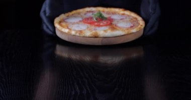 Siyah kauçuk eldivenli erkek ellerinin yakın çekimi erkek aşçı peynirli büyük bir pizza servis ediyor. Domates soslu vejetaryen yemeği, pizza restoranı menüsü konsepti, fast food yakın çekim.
