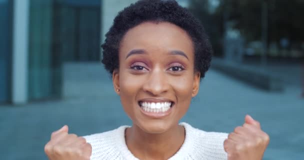 Gai sombre-peau fille afro femme souriant réjouissant victoire debout isolé en plein air célébrer triomphe dit oui cris de bonheur fait geste de victoire avec ses mains profiter de bonnes nouvelles — Video