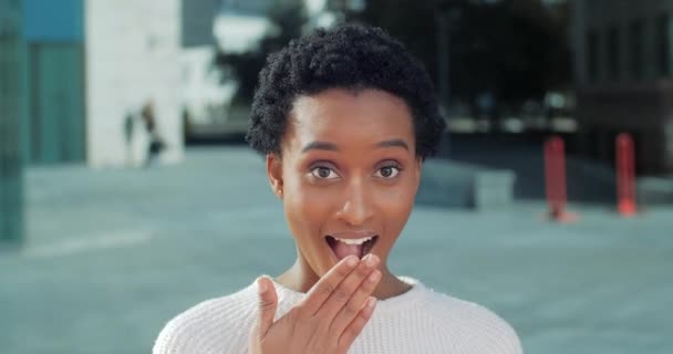 Flört érzelmi vegyes faj nő afro-amerikai lány fehér néz kamera meglepett takarja el a száját a kezét a sokk és öröm megtanulja a titkot lengetve a tenyerét, nő portré szabadban — Stock videók