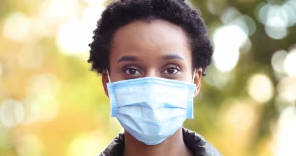 Close-up ernstige donkere huid zwarte jonge vrouw afro-Amerikaanse meisje patiënt dragen beschermende medische masker tegen COVID virus buiten kijken naar camera, veilig reizen na pandemie concept — Stockvideo