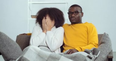 Genç siyahi adam ve Afro-Amerikalı kız çift kanepede oturup televizyon izleyerek korku filmi seyrediyor sinemadaki kadının korkusunu elleriyle saklıyordu.