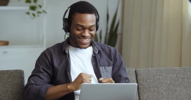 Retrato close-up afro americano cara negro homem de negócios estudante sentado descansando sozinho em casa no sofá usa fones de ouvido relógios clipes de vídeo on-line ouvir melodias música dançando aplausos dedos — Vídeo de Stock