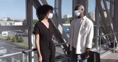 Tıbbi maskeli üzgün çift Afro-Amerikalı koca ve genç kıvırcık saçlı kadın havaalanı terminalinde ellerinde biletlerle bekliyorlar. Uçuş iptali hakkında kötü haberler öğreniyorlar.